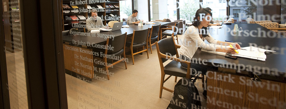 Students studying in the library behind a glass wall with white lettering. 