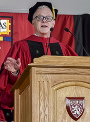 Neal Baer speaking at a podium dressed in a cap and gown.