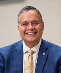 Man wearing a blue suit jacket and yellow tie smiling at the camera.