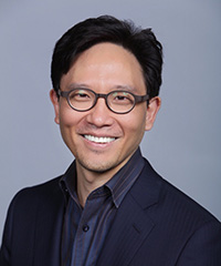 Man with glasses and a dark suit smiling at the camera.