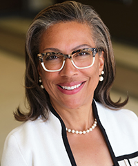 Woman wearing glasses and a pearl necklace smiling at the camera.