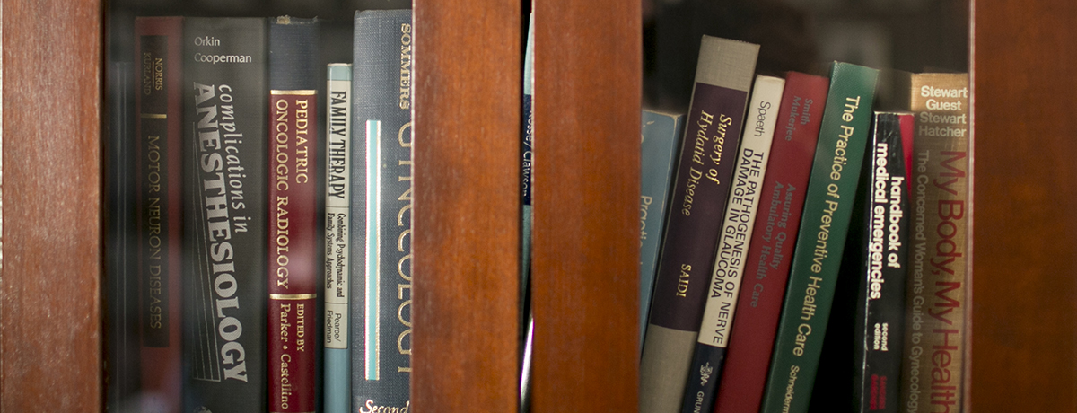 Photo of medical books on a shelf behind glass.