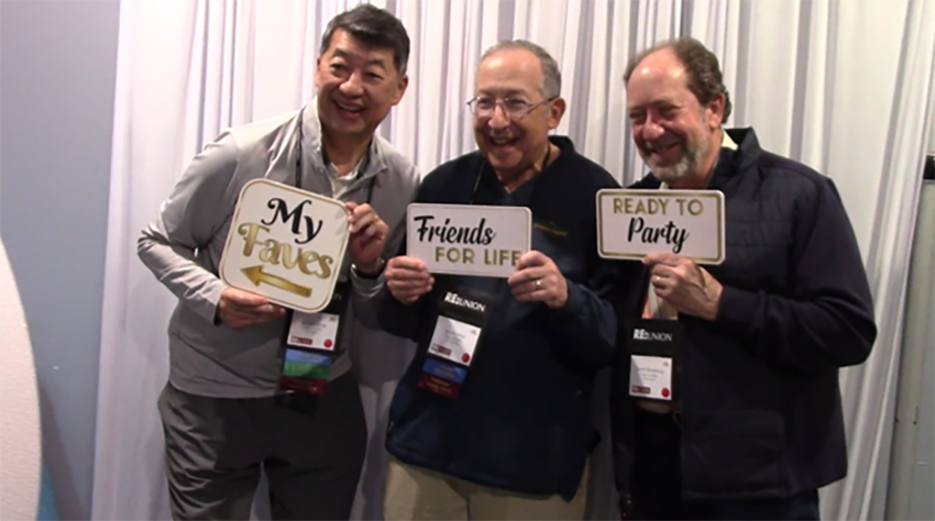3 alum smiling holding up signs 